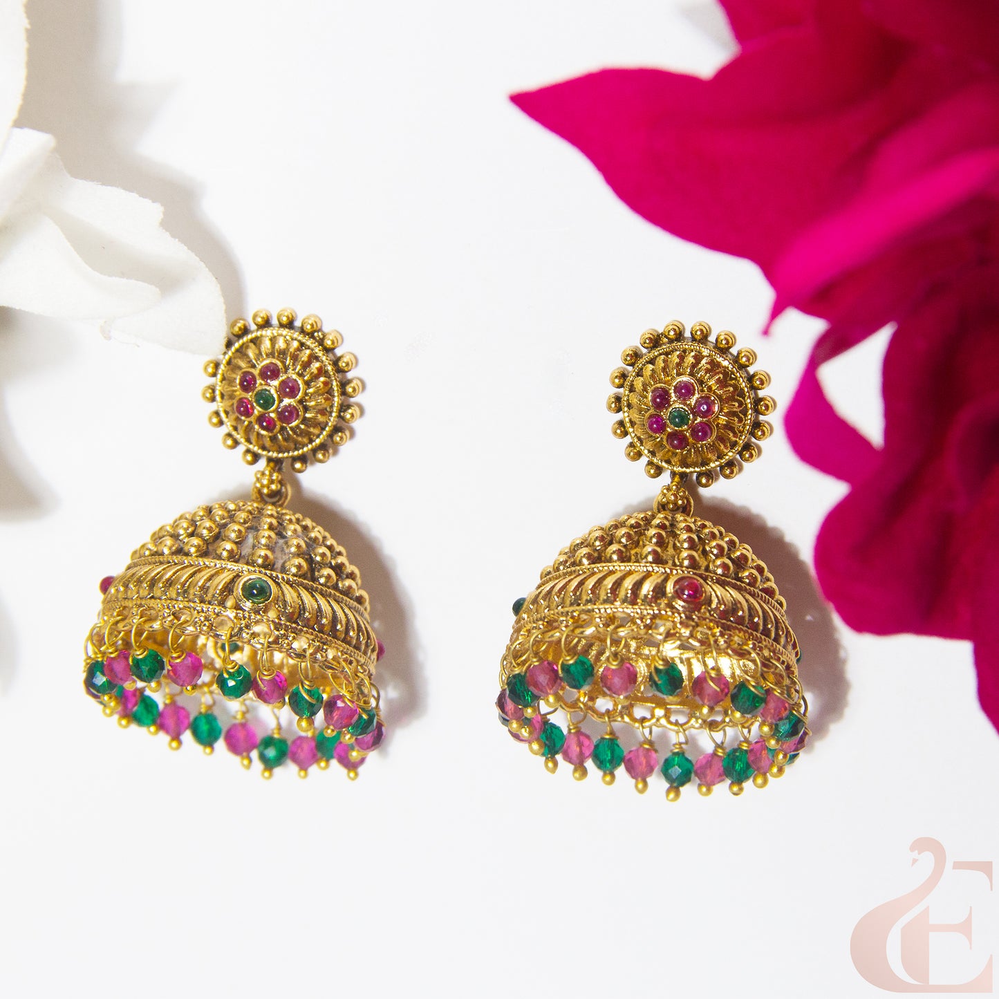 Gold earrings with colorful gemstones on a white background with pink flowers.