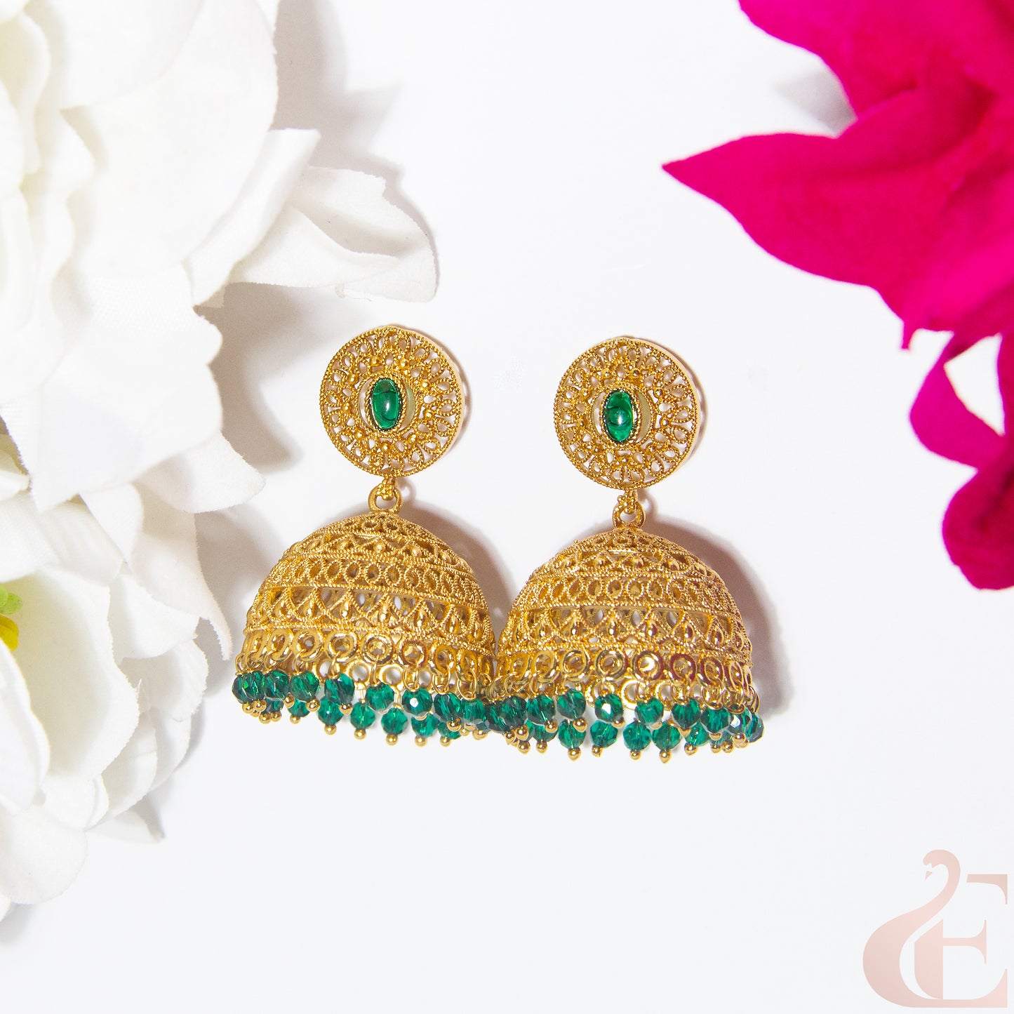 Gold earrings with green gemstones on a white background with pink flowers.