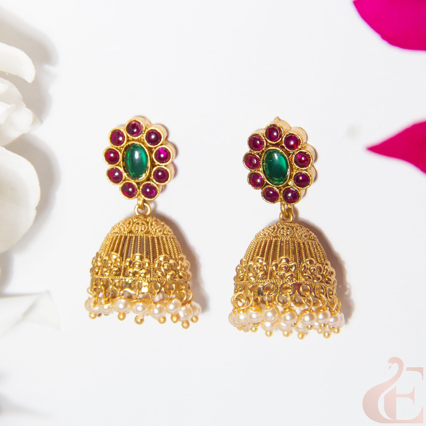 Gold jhumka earrings with green and ruby stones on a white background