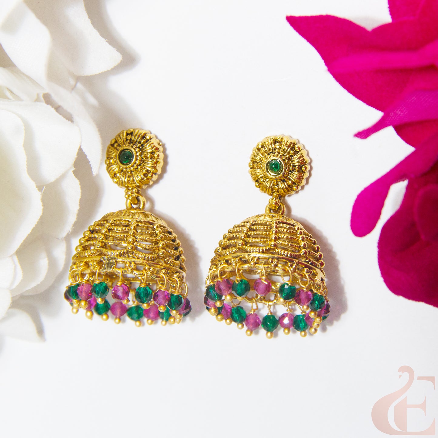 Gold earrings with green and ruby gemstones on a white background with pink flowers.