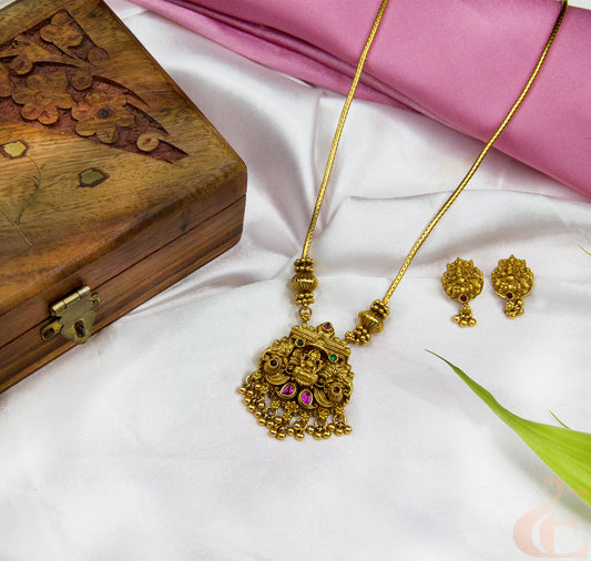 Gold necklace and earrings on a white surface with a wooden box and pink fabric in the background.