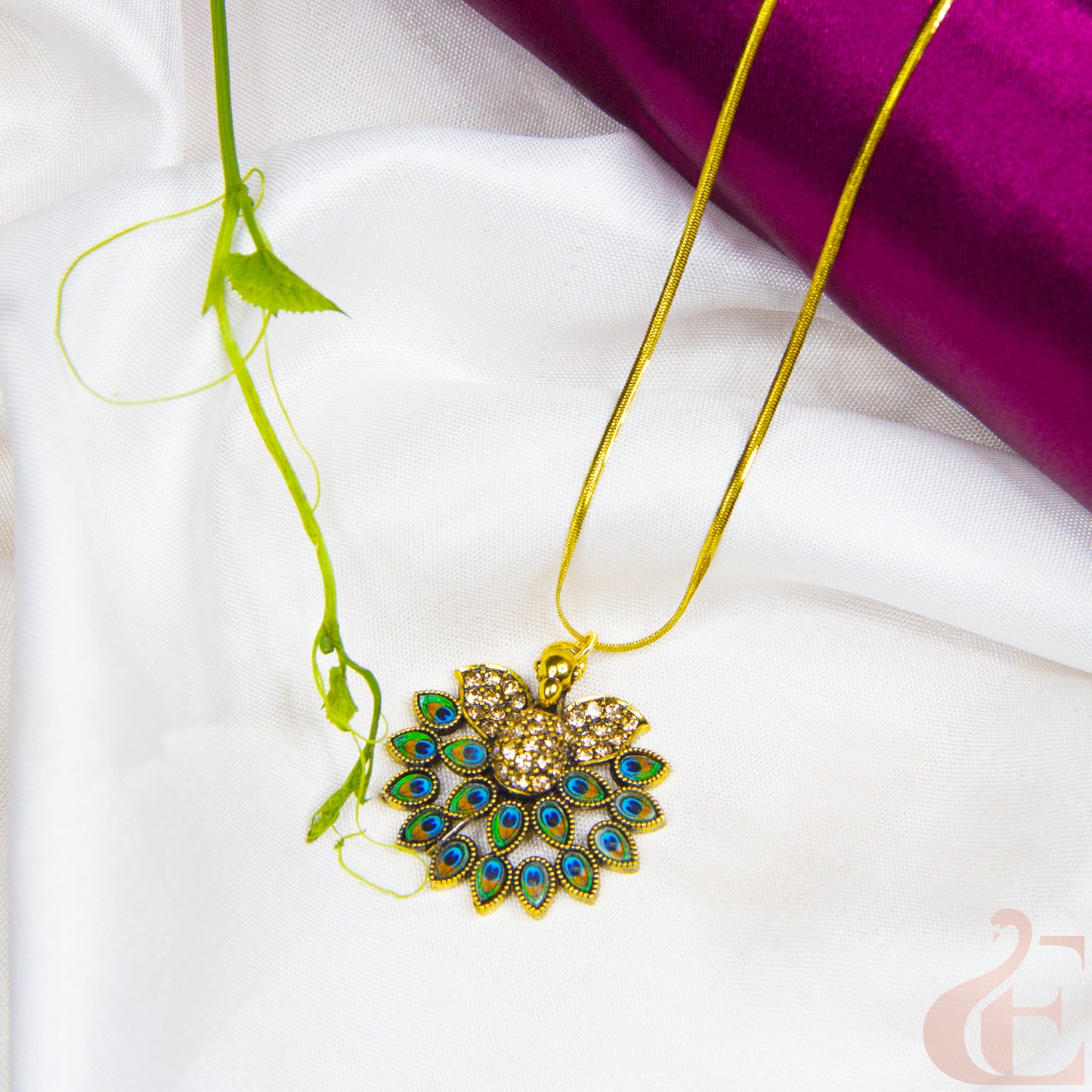 Gold necklace with a peacock feather pendant on a white and purple fabric background
