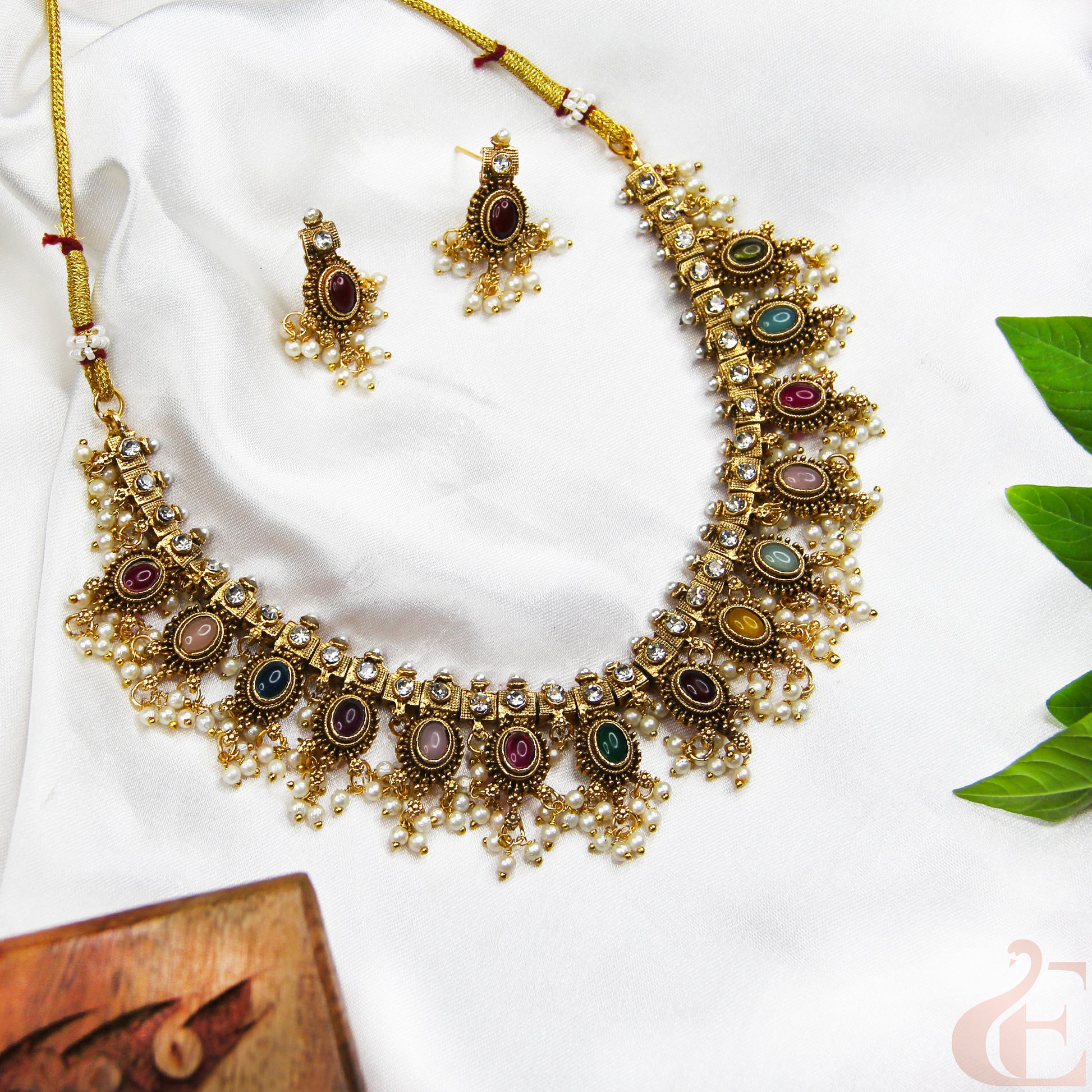 Ornate gold necklace with colorful stones and matching earrings on a white background