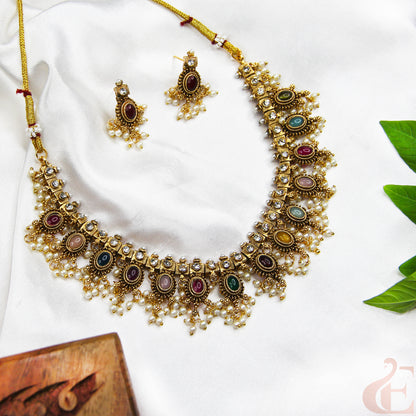 Ornate gold necklace with colorful stones and matching earrings on a white background
