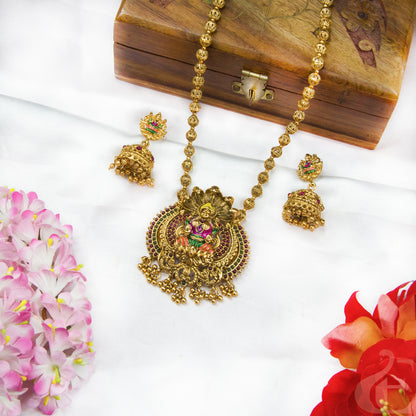 Gold necklace and earrings set on a white surface with flowers and a wooden box.