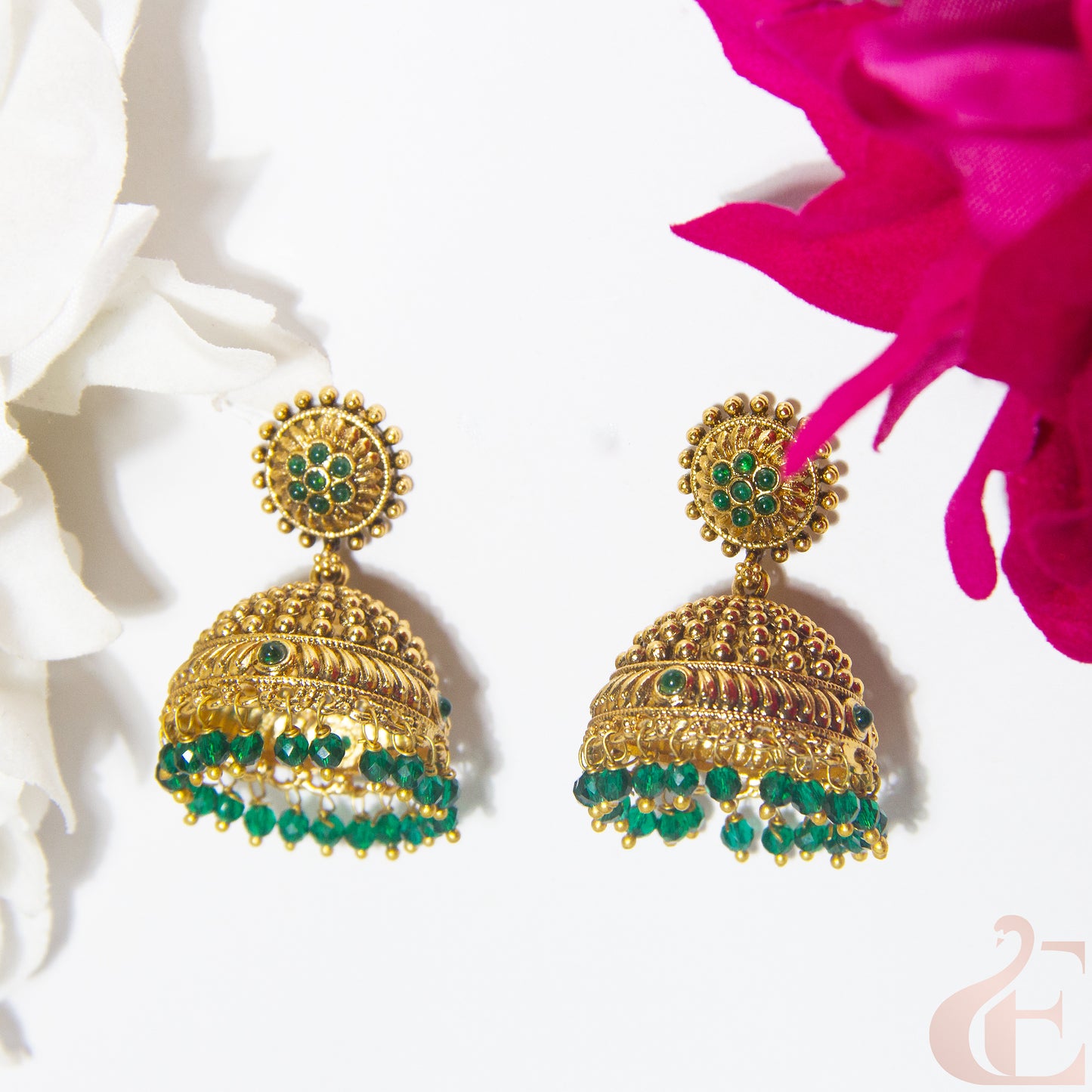 Gold earrings with green beads on a white background with pink flowers.