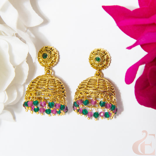Gold earrings with green and ruby gemstones on a white background with pink flowers.