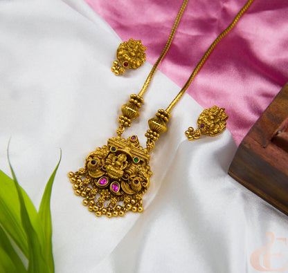 Gold necklace and earrings on a white fabric background with a pink cloth underneath