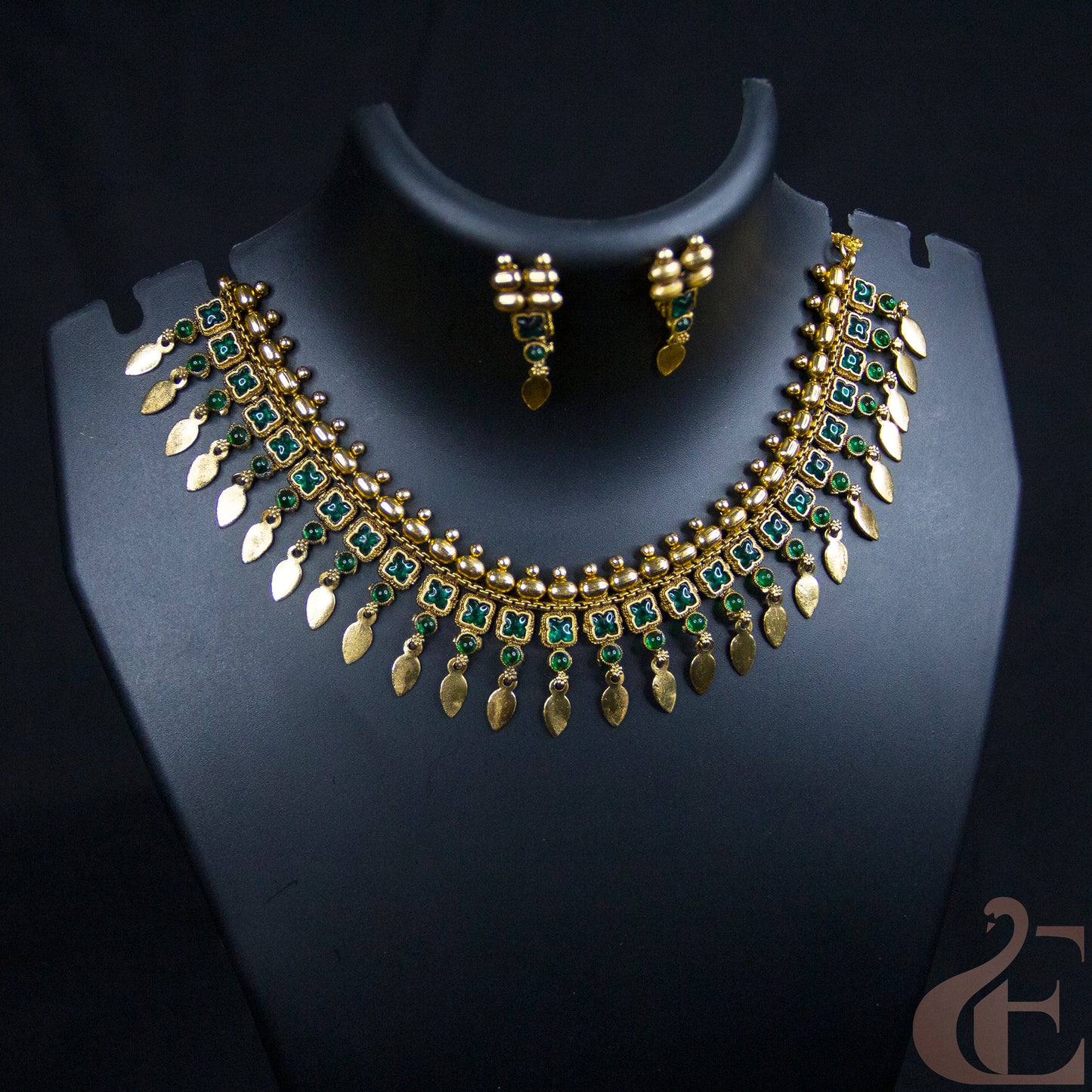 Gold-plated Indian style necklace and matching earrings set with green stone accents, displayed on a black jewelry bust.