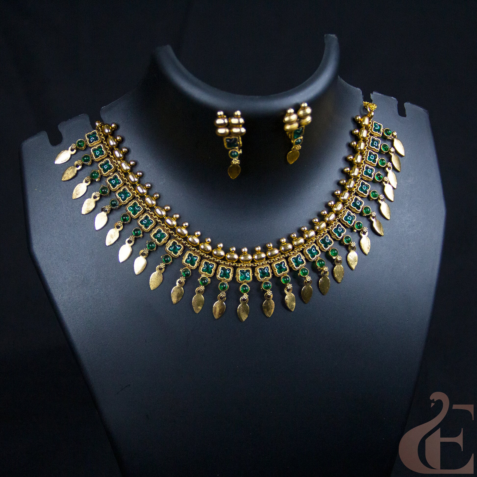 Gold-plated Indian style necklace and matching earrings set with green stone accents, displayed on a black jewelry bust.