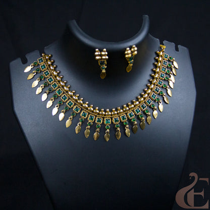 Gold-plated Indian style necklace and matching earrings set with green stone accents, displayed on a black jewelry bust.