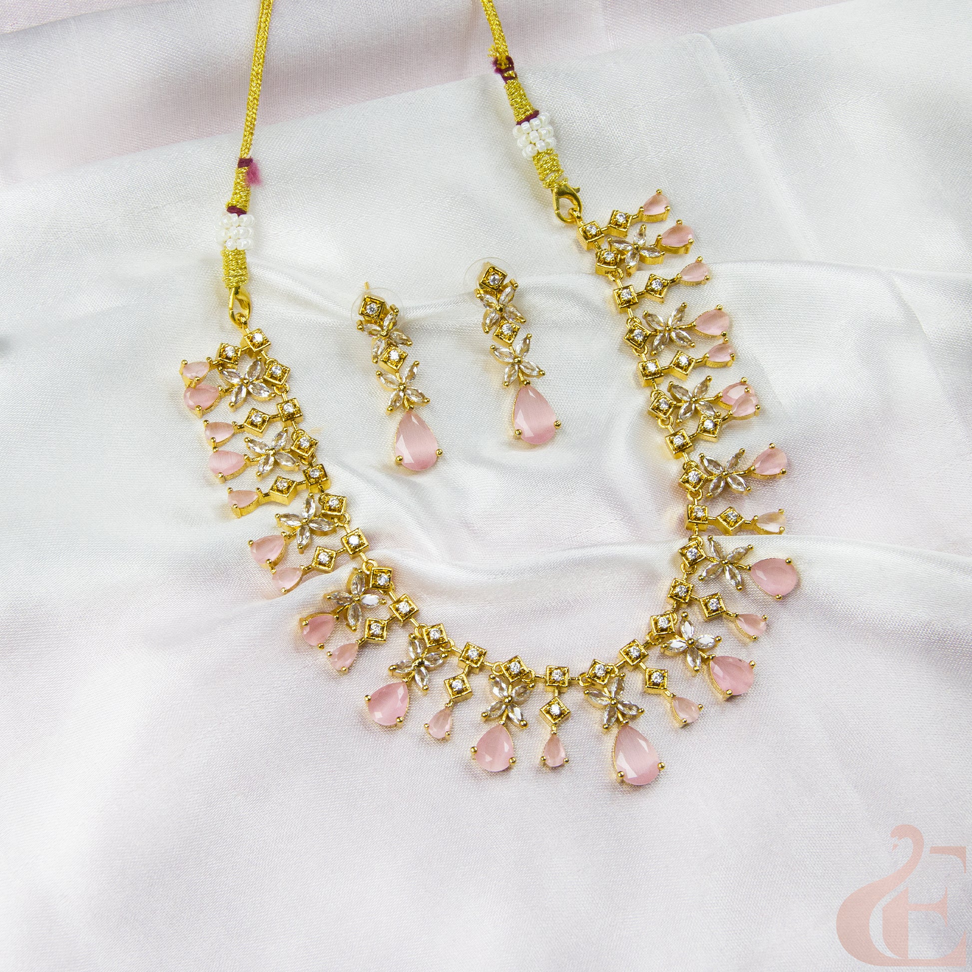 Gold necklace with pink stones and matching earrings on a white fabric background