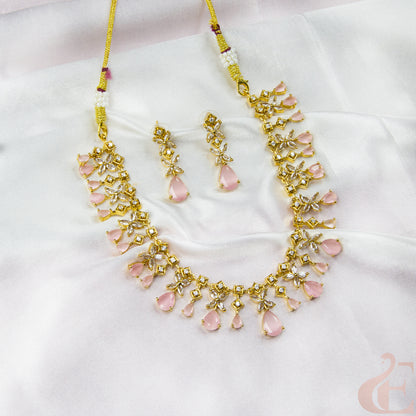 Gold necklace with pink stones and matching earrings on a white fabric background