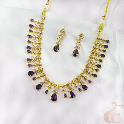 Gold necklace with purple stones and matching earrings on a white background