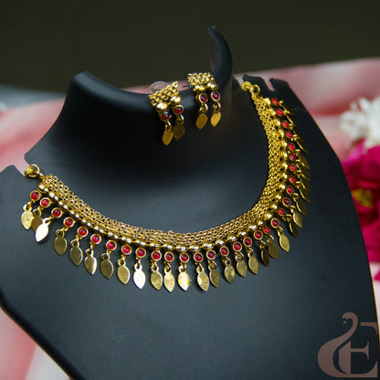 Gold-toned traditional necklace and matching earrings displayed on a black jewelry bust. The necklace features a layered chain design with dangling gold leaf-shaped charms and small red stone accents.