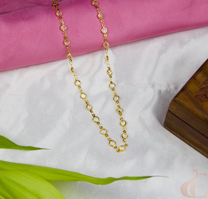Gold chain necklace on a white surface with pink fabric in the background