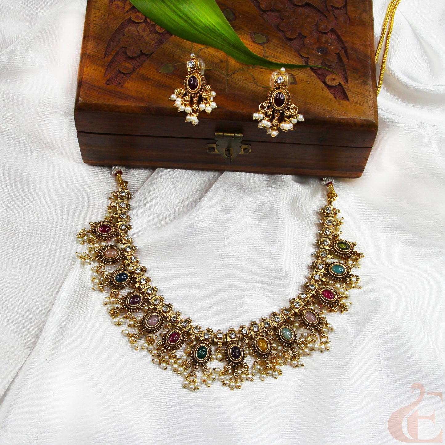 Gold necklace with colorful stones and matching earrings on a wooden box.