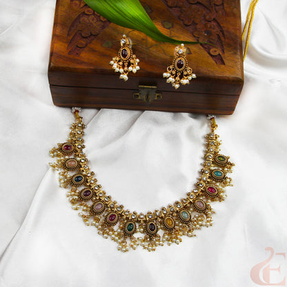 Gold necklace with colorful stones and matching earrings on a wooden box.