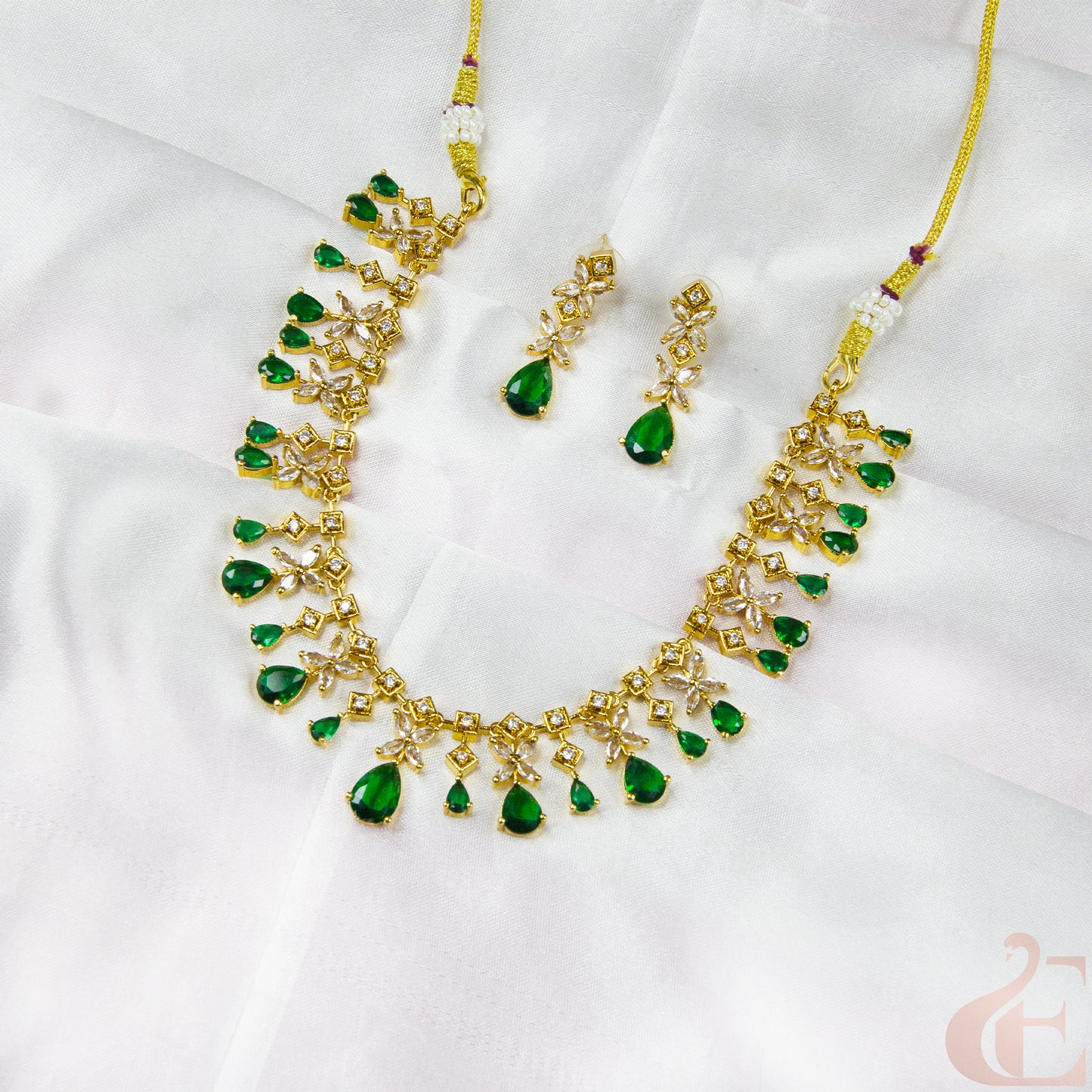 Gold necklace with green gemstones on a white fabric background