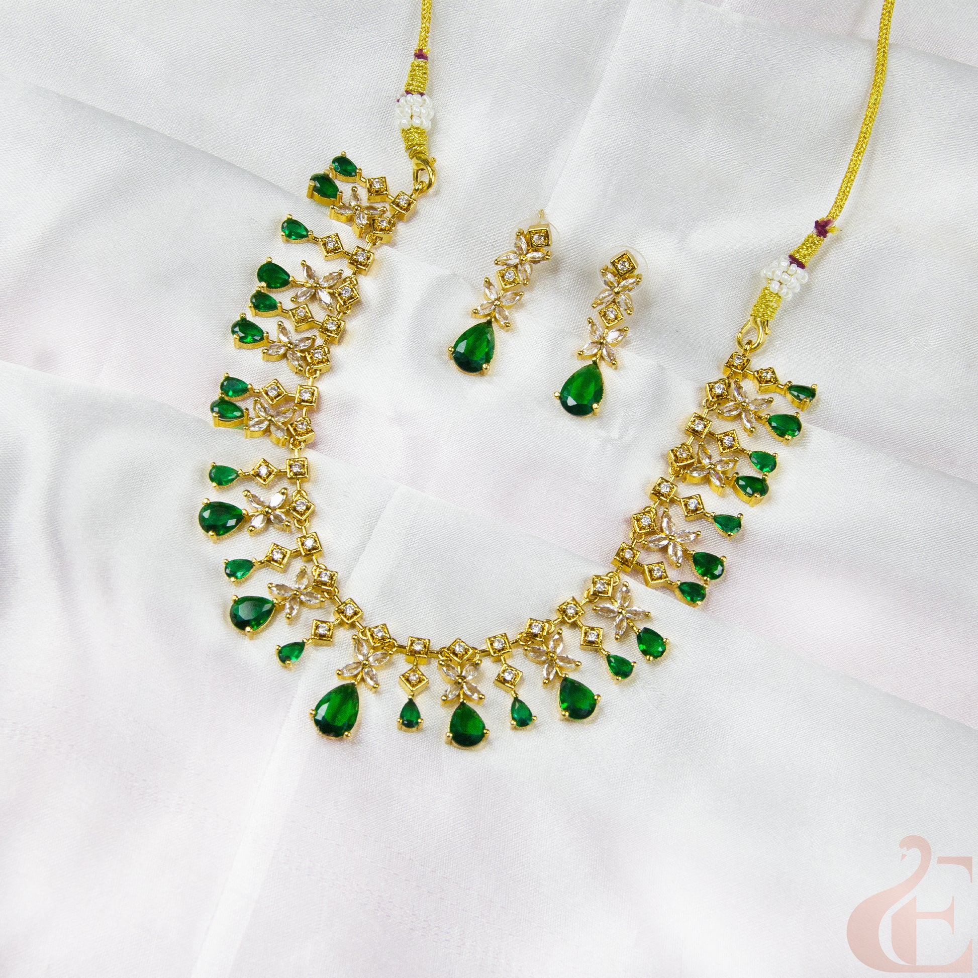 Gold necklace with green gemstones on a white fabric background