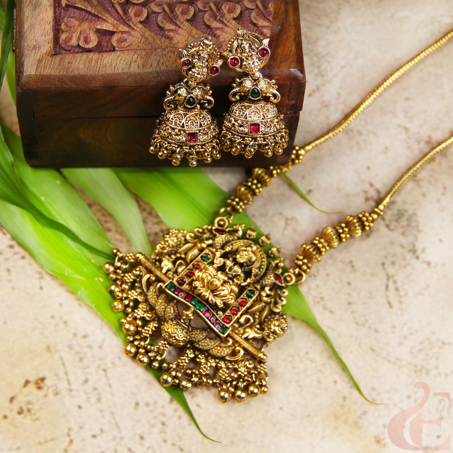Gold necklace and earrings on a textured surface with green leaves