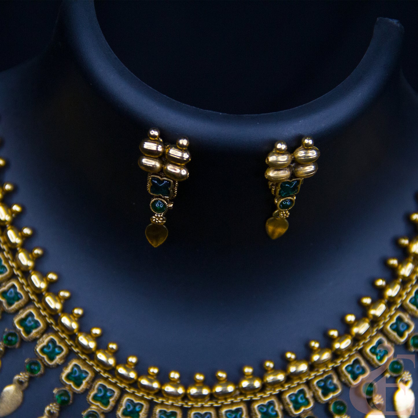 Gold-plated jewelry set featuring a multi-strand necklace and matching earrings with green enamel accents, displayed on a dark blue jewelry bust.
