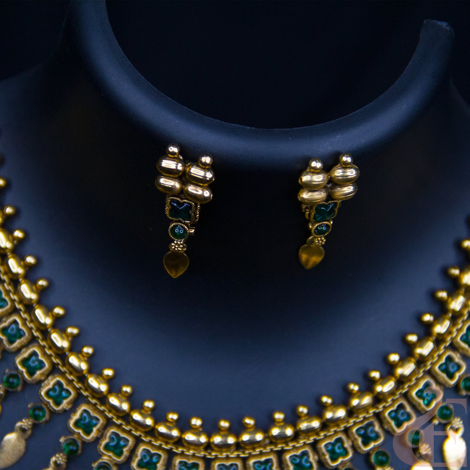 Gold-plated jewelry set featuring a multi-strand necklace and matching earrings with green enamel accents, displayed on a dark blue jewelry bust.