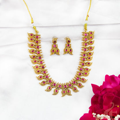 Gold necklace with pink stones and matching earrings on a white background with a red flower.