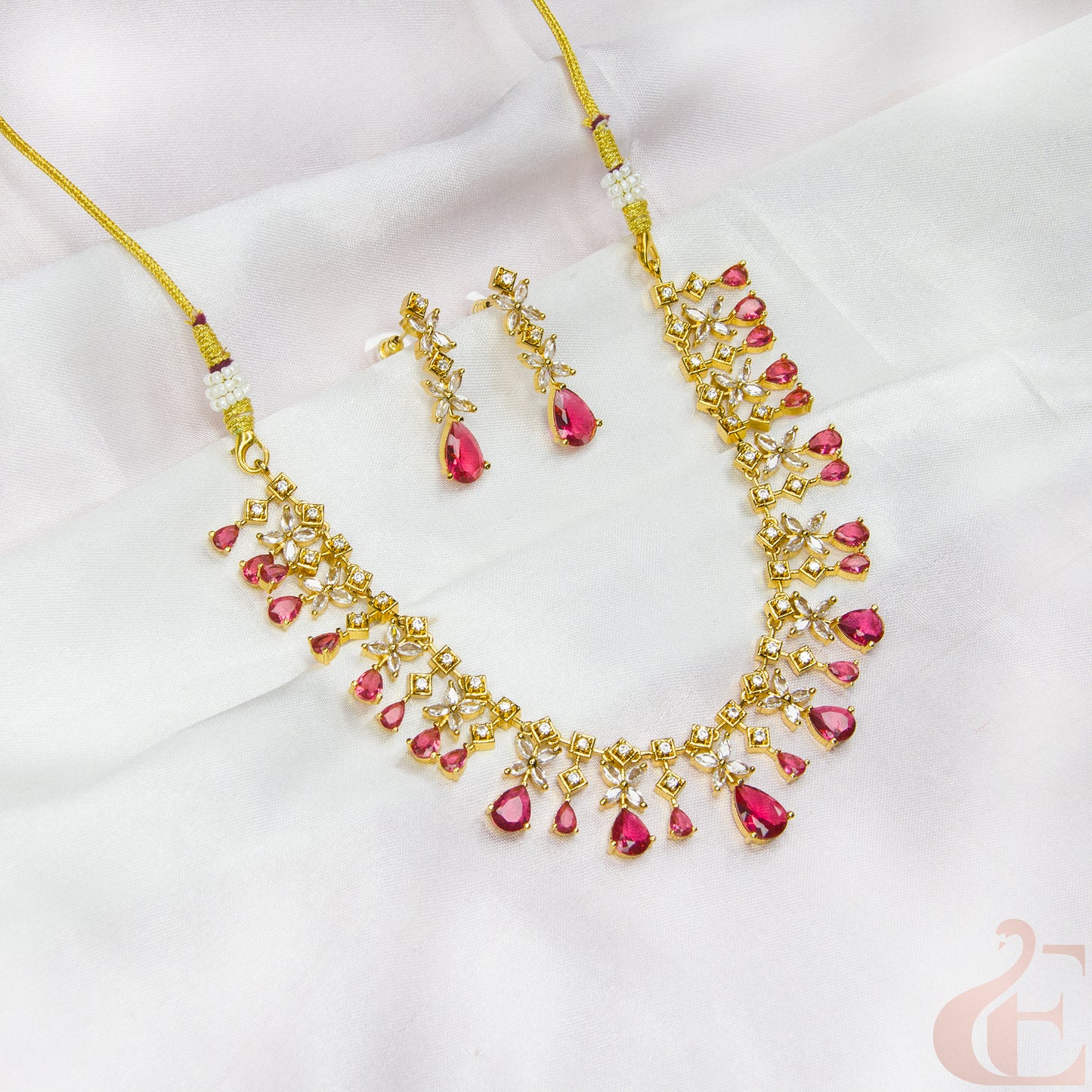 Gold necklace with pink stones and matching earrings on a white background
