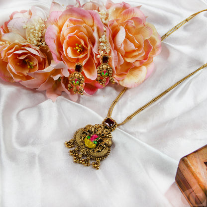 Ornate necklace and earrings on a white fabric background with pink flowers.