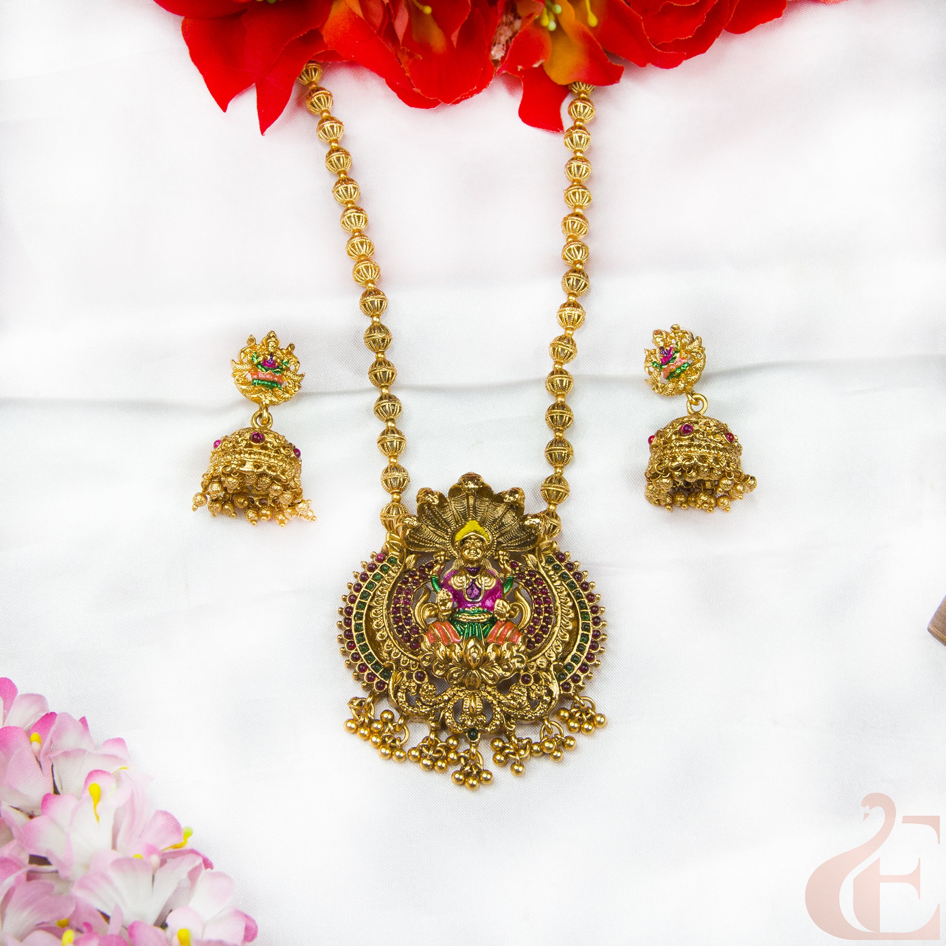 Gold necklace with pendant and earrings on a white background with flowers.
