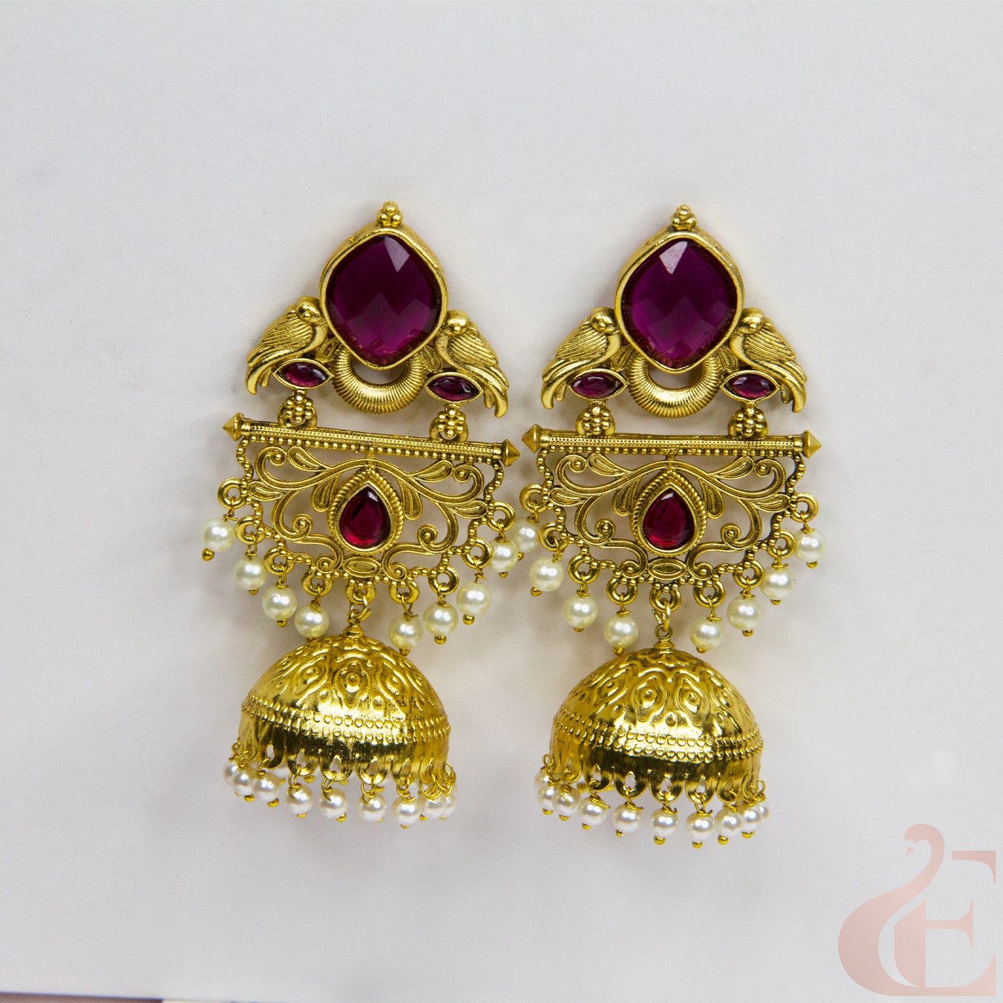 Gold earrings with red gemstones and pearl accents on a light gray background
