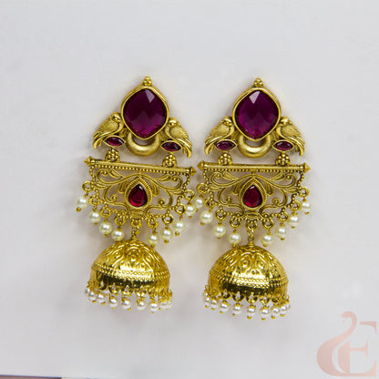Gold earrings with red gemstones and pearl accents on a light gray background
