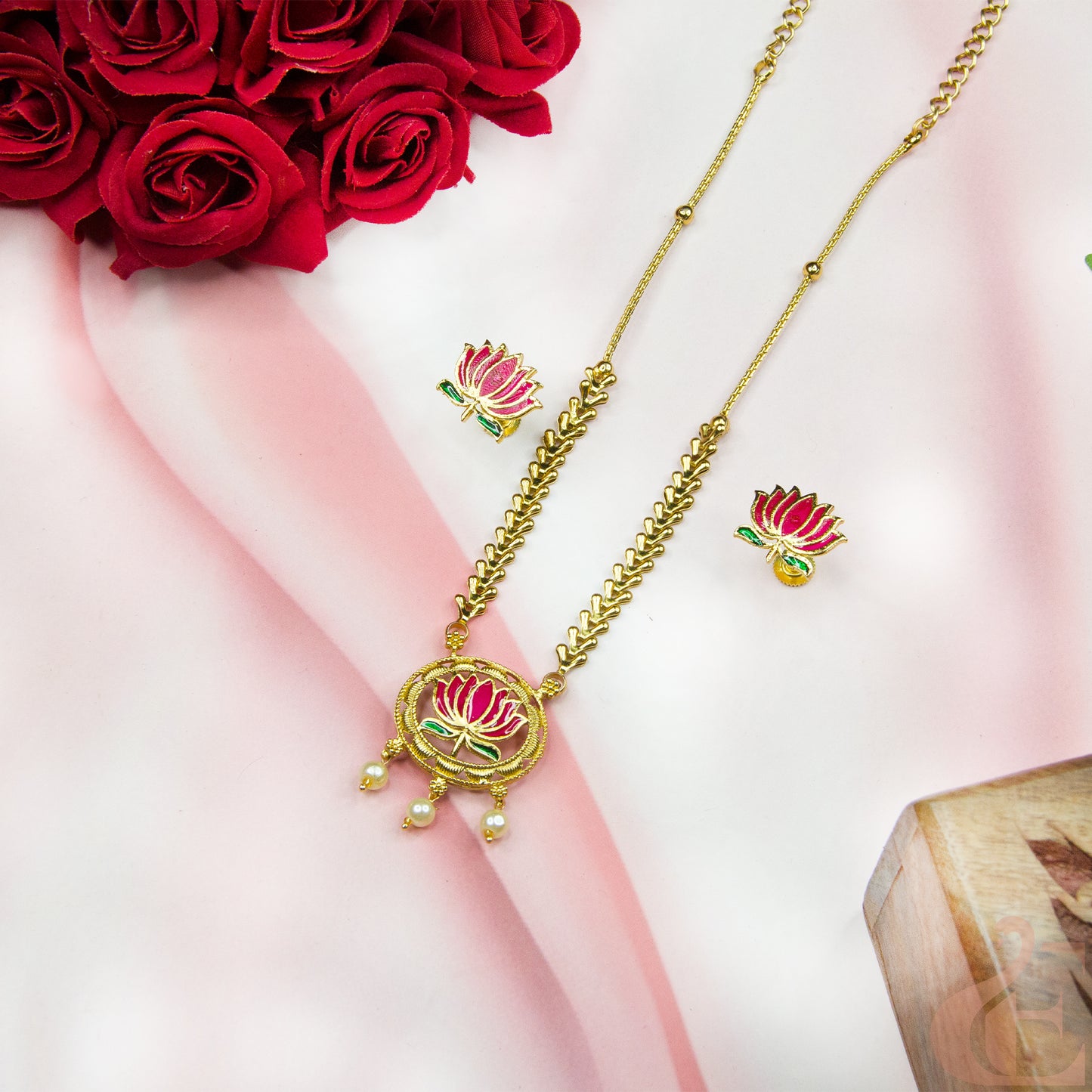Gold necklace with floral design and matching earrings on a pink fabric background with red roses.