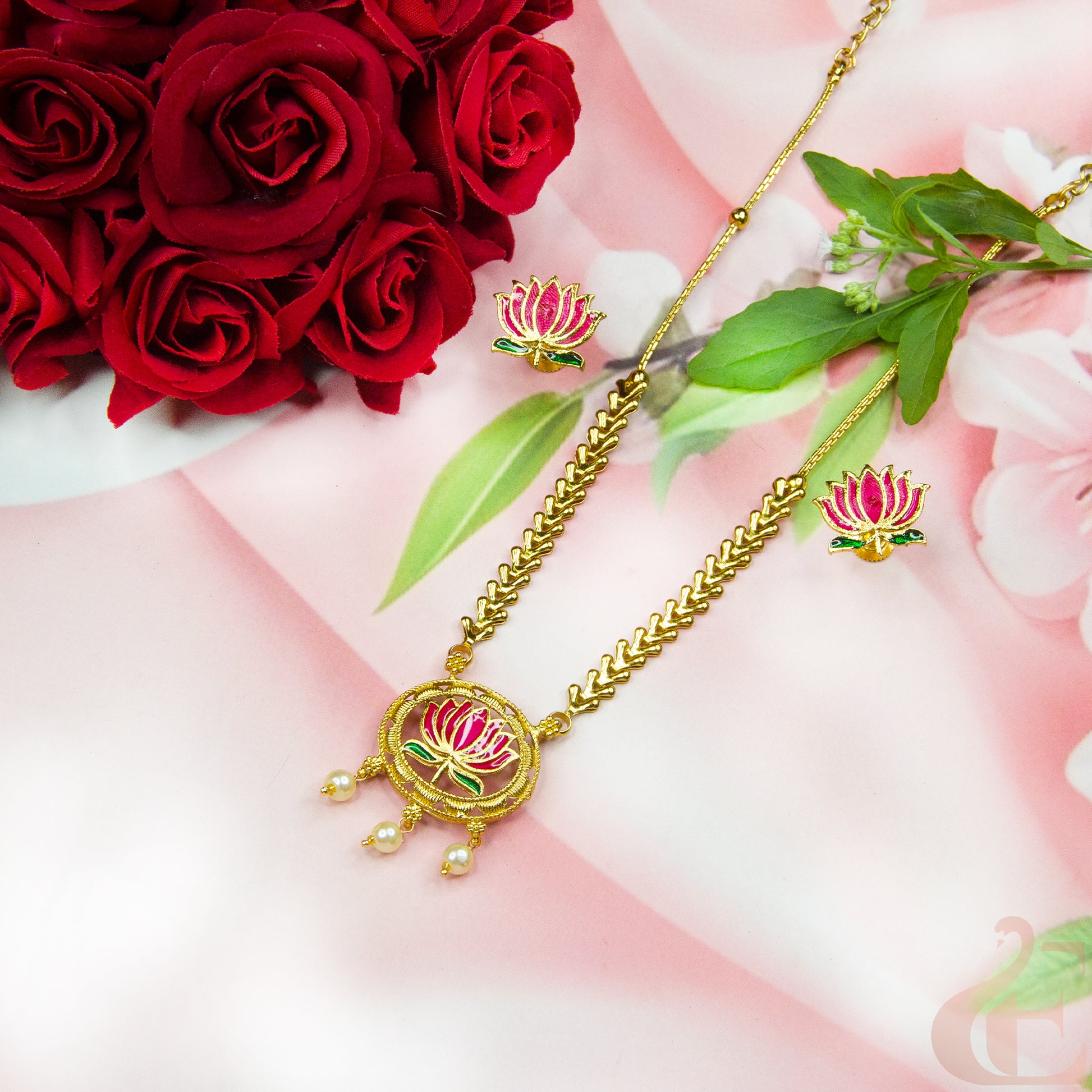 Gold necklace with floral design on a pink fabric background with red roses and green leaves.