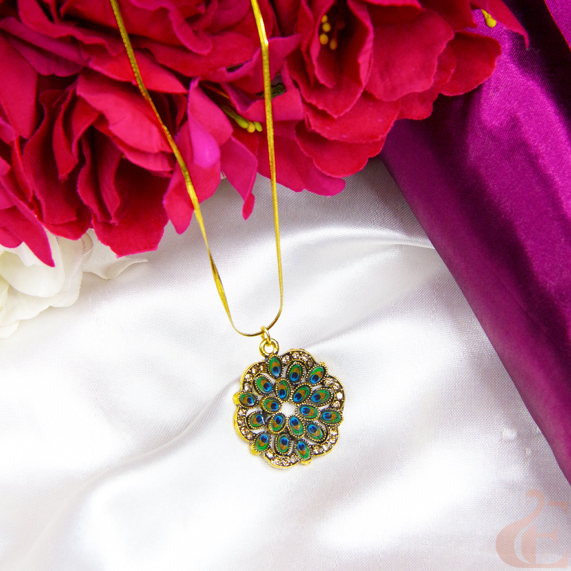 Decorative necklace with a green and gold pendant on a white fabric background with red flowers.