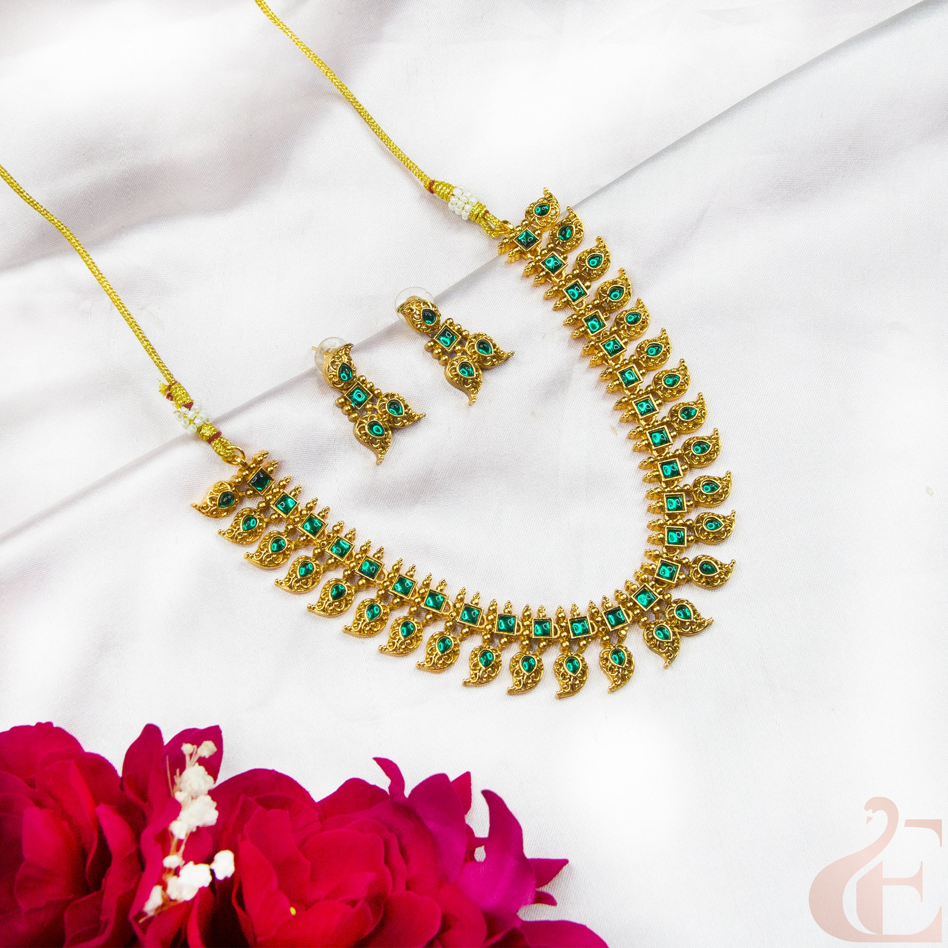 Gold necklace with green stones and matching earrings on a white fabric background with pink flowers.