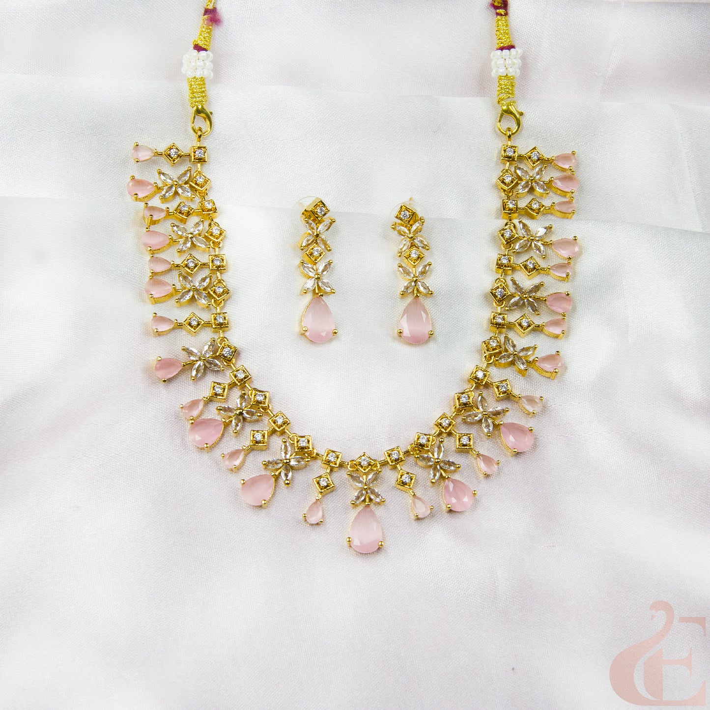 Gold necklace and earrings with pink stones on a white background