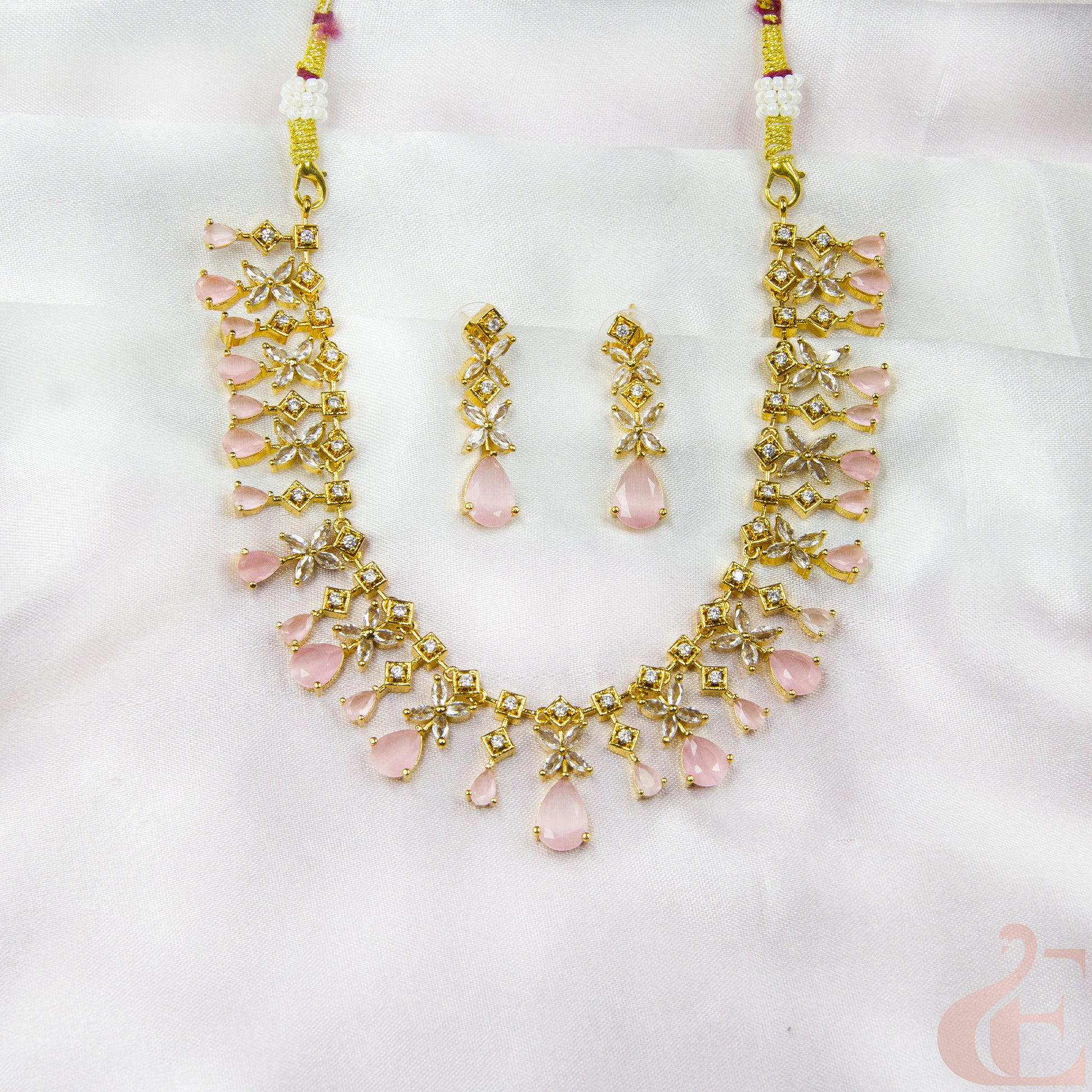 Gold necklace and earrings with pink stones on a white background