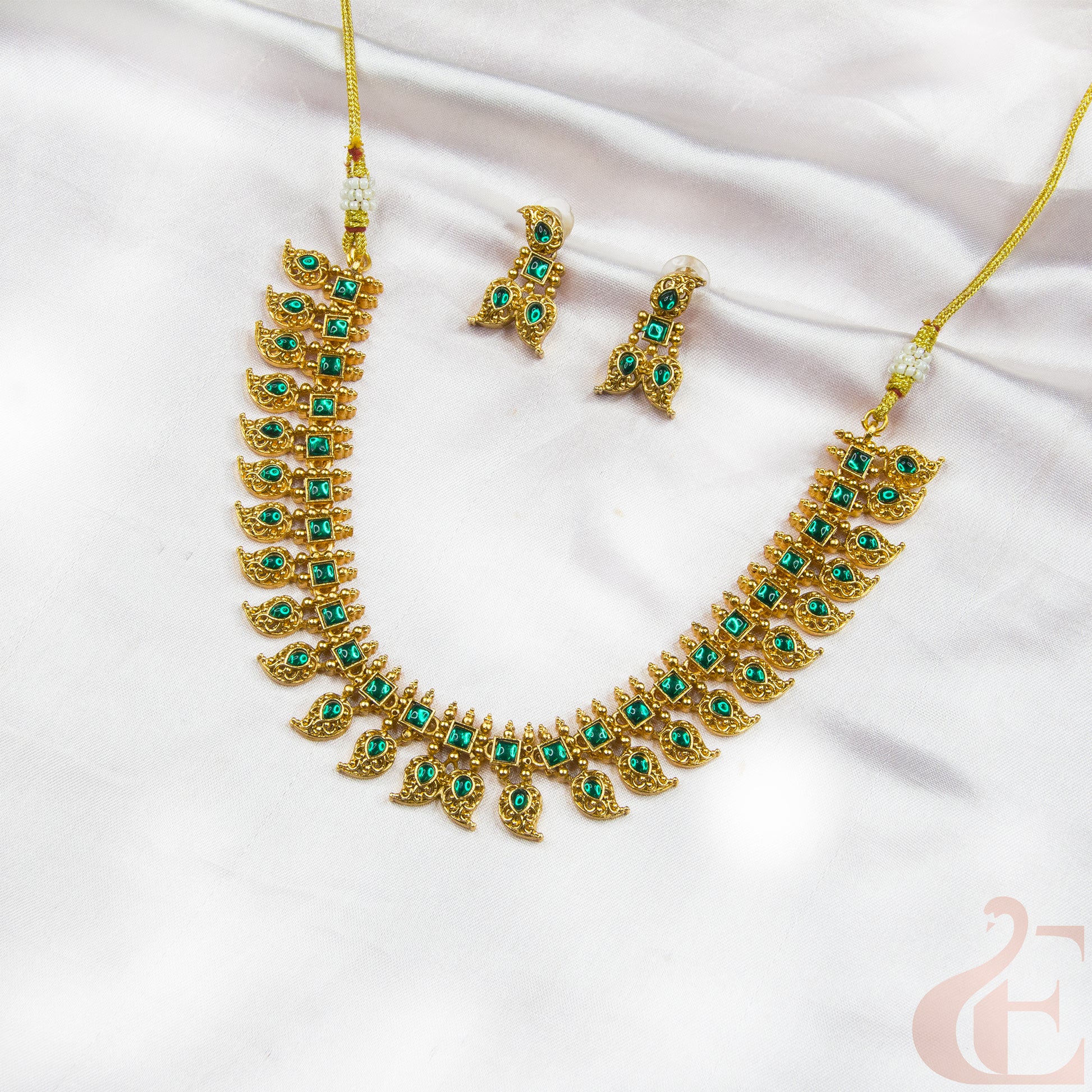 Gold necklace with green gemstones and matching earrings on a white fabric background