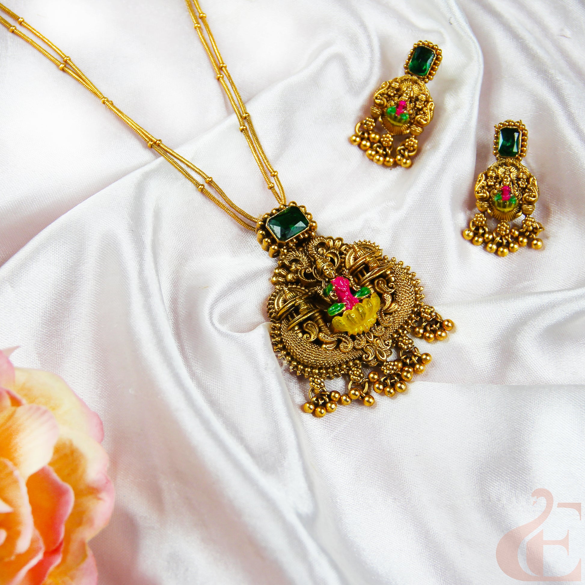 Gold necklace and earrings with green gemstones on a white fabric background