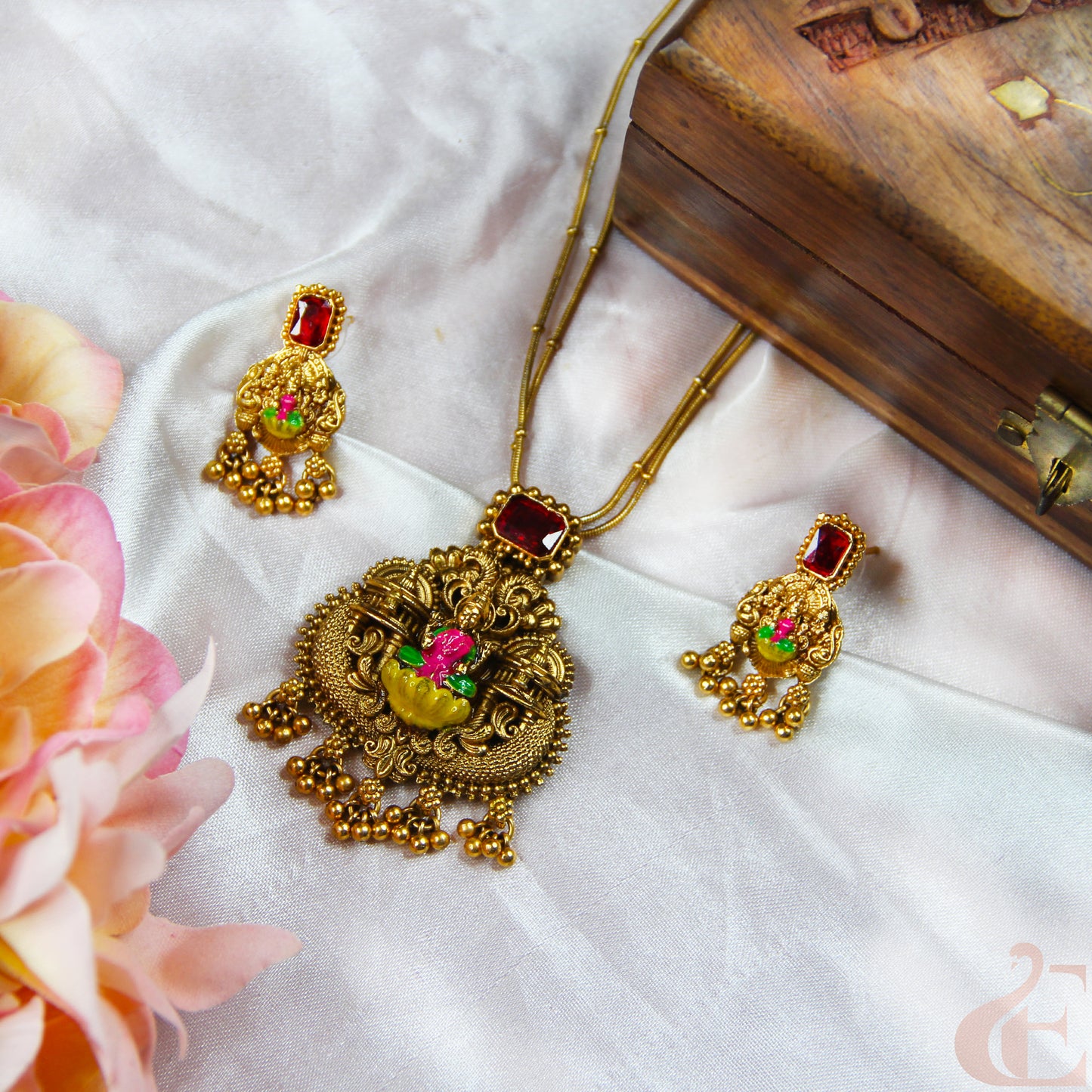 Gold necklace with red gemstones and matching earrings on a white fabric background