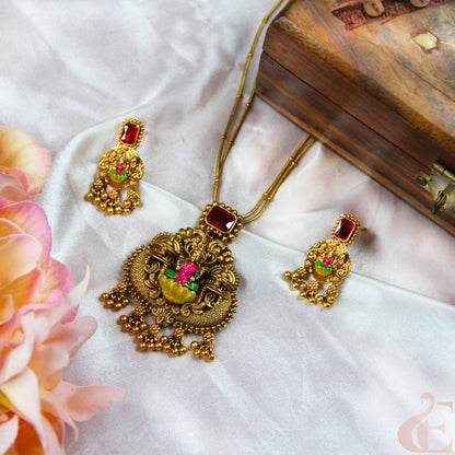 Gold necklace with red gemstones and matching earrings on a white fabric background