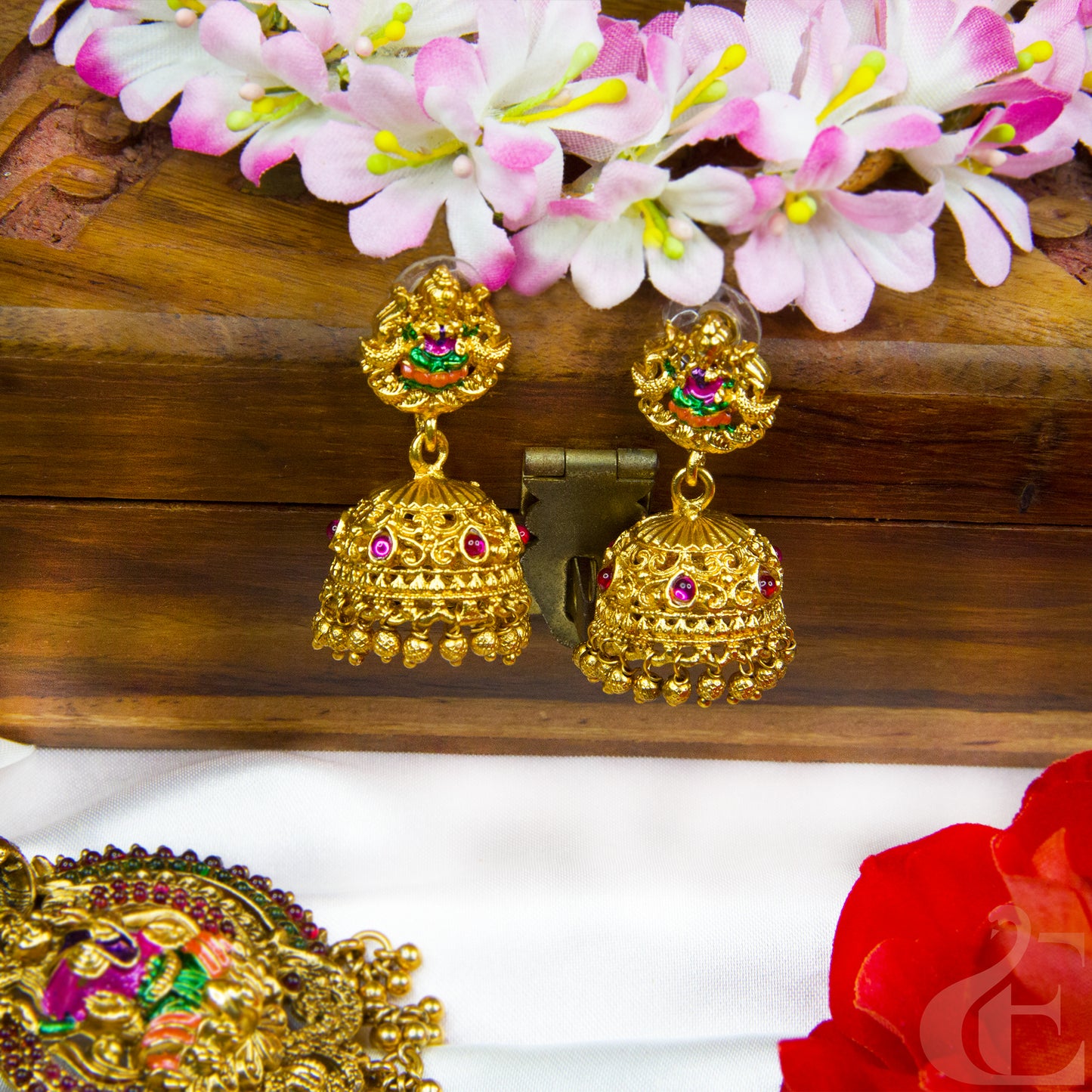 Gold earrings with gemstones on a wooden surface with flowers