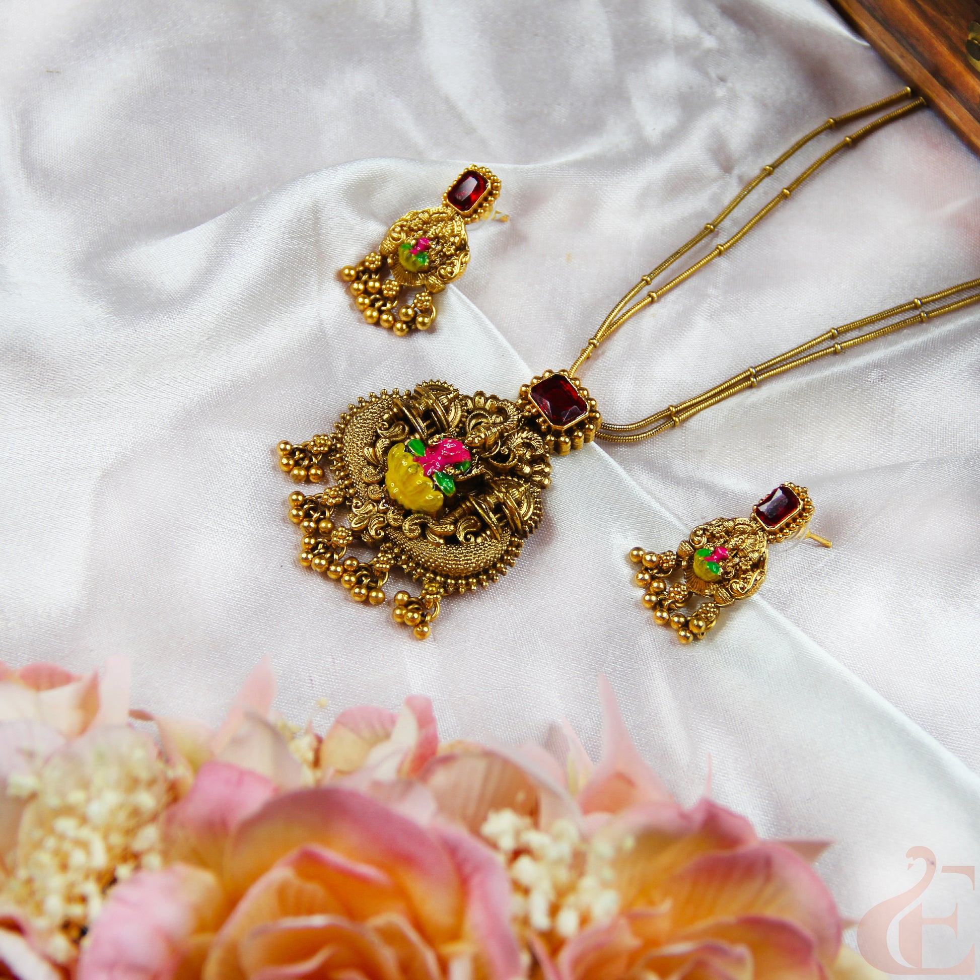 Gold necklace with red and green gemstones on a white fabric background with flowers.