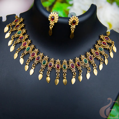 Gold-toned traditional jewelry set featuring a statematching earrings, ment necklace and embellished with red and green stones on a black display bust.