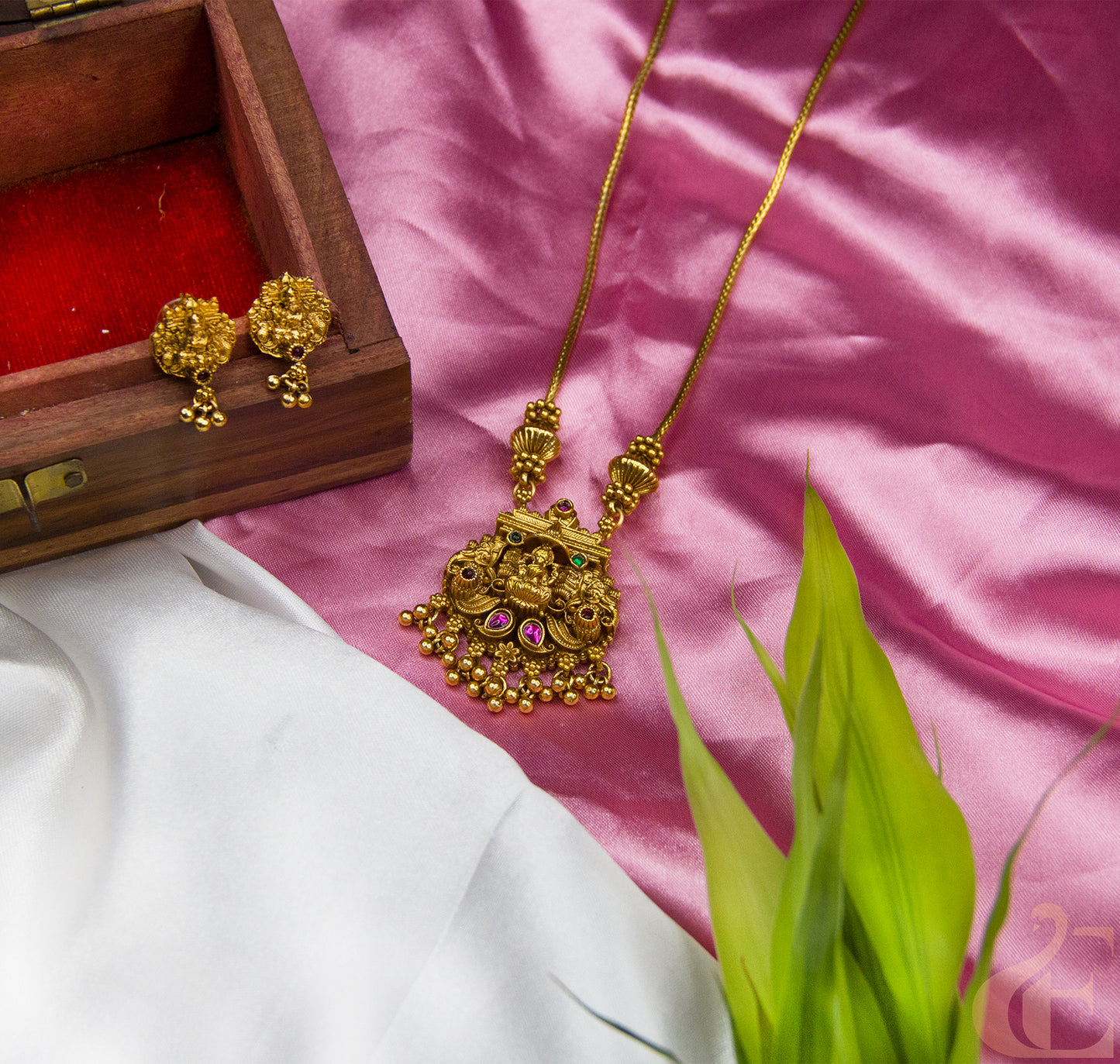 Gold necklace and earrings on a pink fabric background with a wooden box.