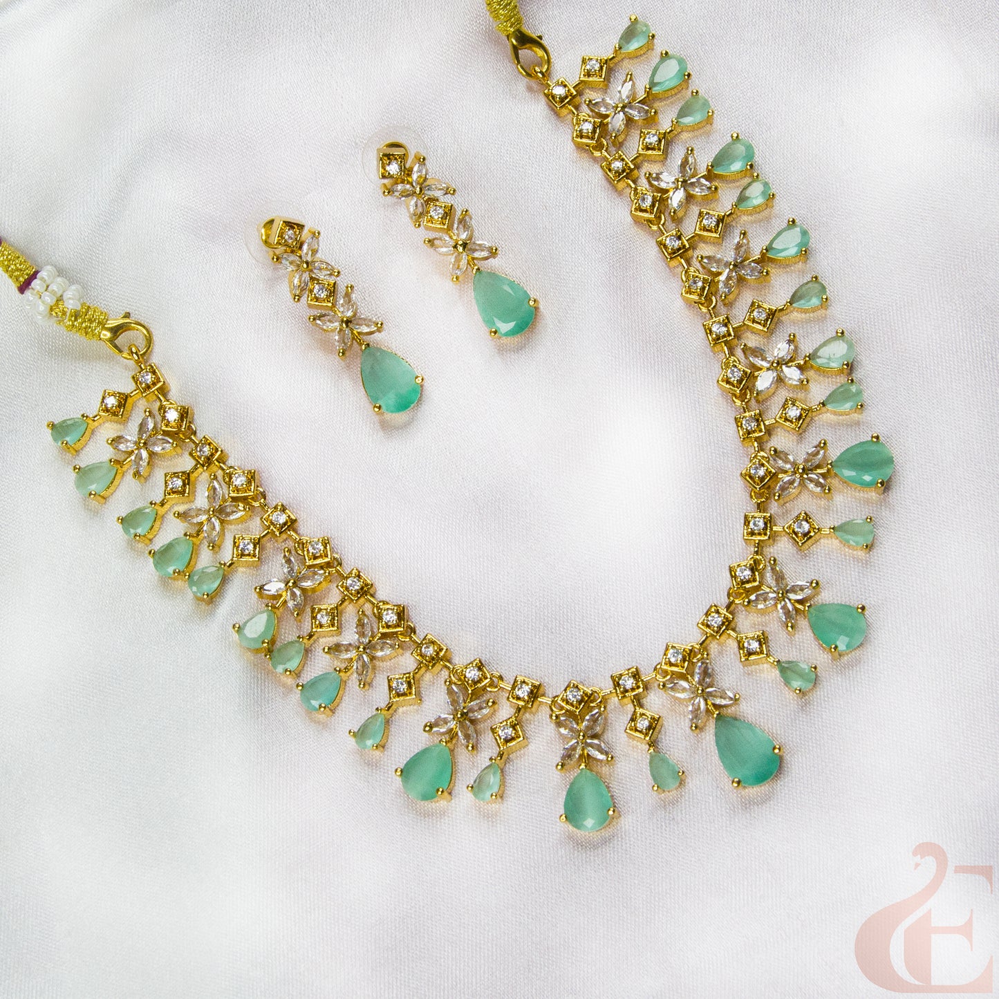 Gold necklace with green gemstones and matching earrings on a white background
