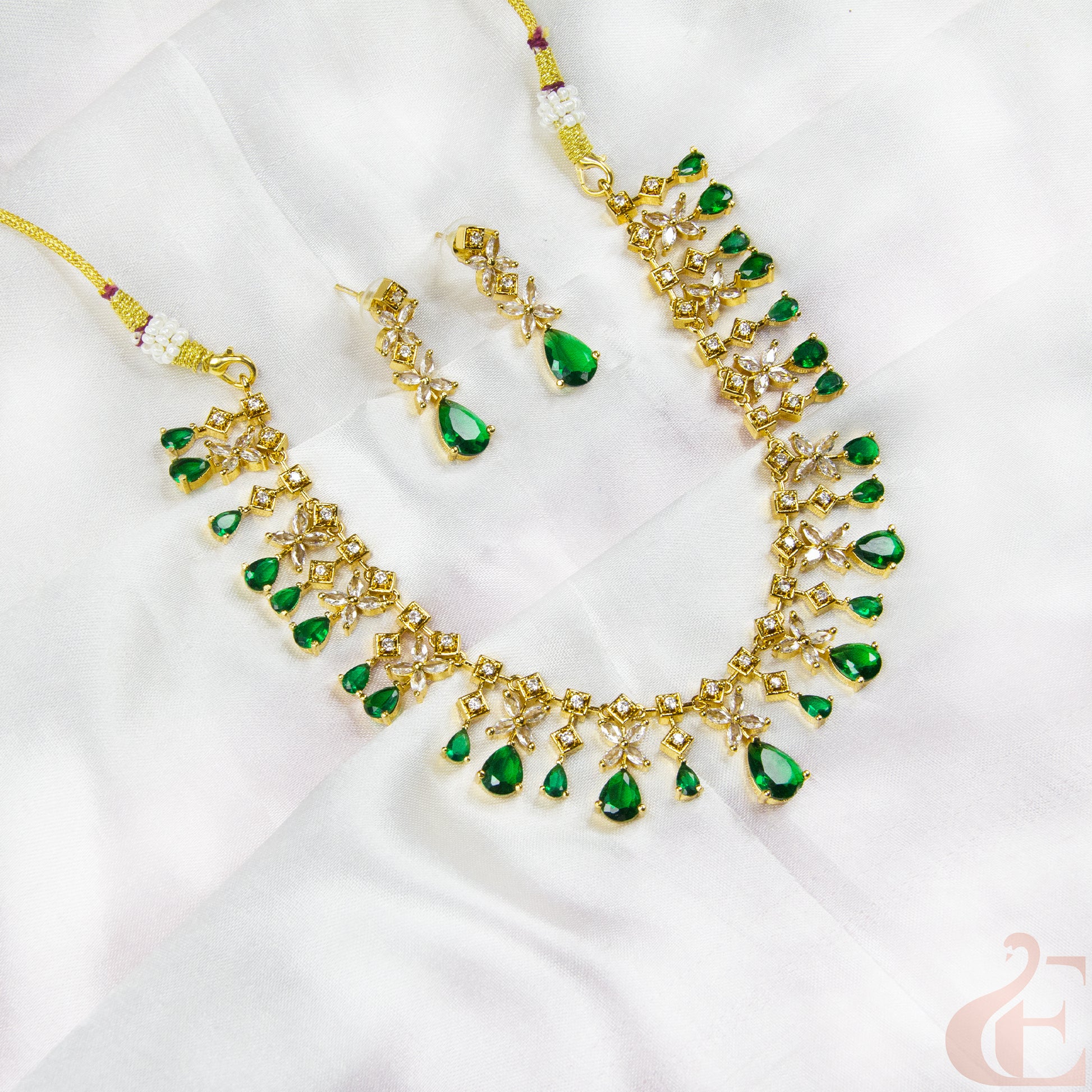 Gold necklace with green gemstones and matching earrings on a white fabric background