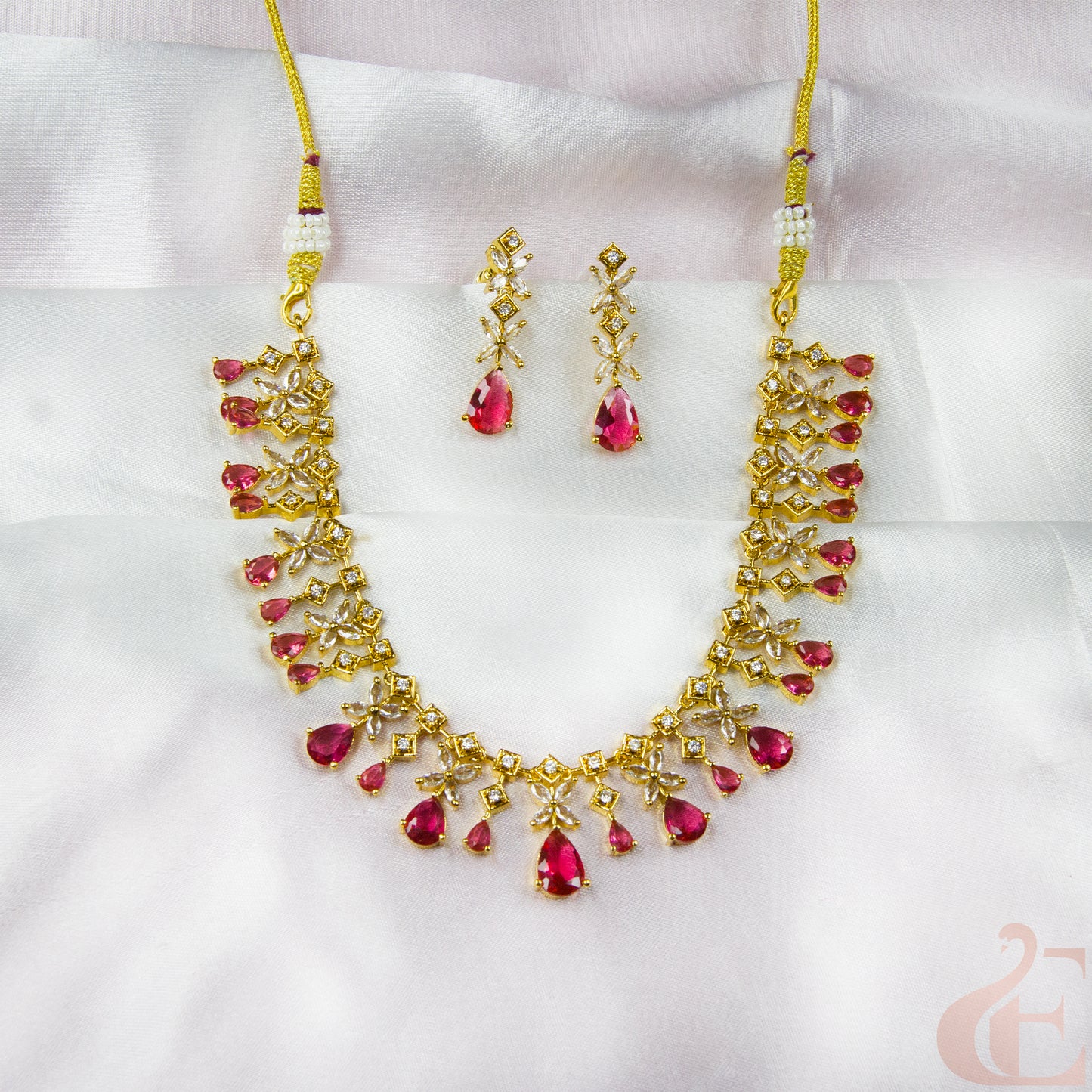 Gold necklace with red gemstones and matching earrings on a white background